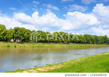 embankment of a river uzh in summer. longest linden alley in europe on a sunny day. view of lush trees near water under blue sky with clouds. beautiful urban landscape of ukraine for travel 128584639