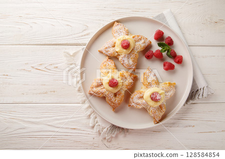 Vanilla puff pastries filled with delicate custard cream and fresh raspberries close-up in a plate. Horizontal top view Vanilla puff pastries filled with delicate custard cream and fresh raspberries close-up in a plate. Horizontal top view 128584854