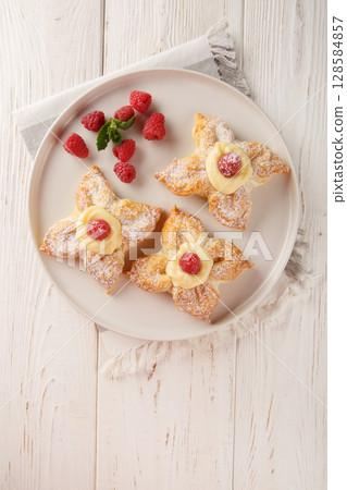 Sweet puff pastry with vanilla custard and fresh raspberries close-up in a plate. Vertical top view 128584857
