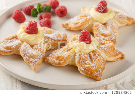 Festive puff pastries filled with vanilla custard and fresh raspberries close-up in a plate. Horizontal 128584862