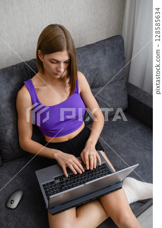 Focused young woman working on laptop at home on sofa. Focused young woman working on laptop at home on sofa. 128585634