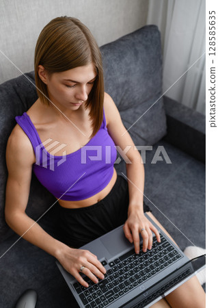 Focused young woman working on laptop at home on sofa. Focused young woman working on laptop at home on sofa. 128585635