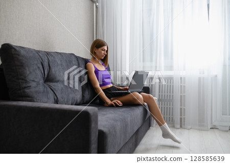 Focused young woman working on laptop at home on sofa. 128585639