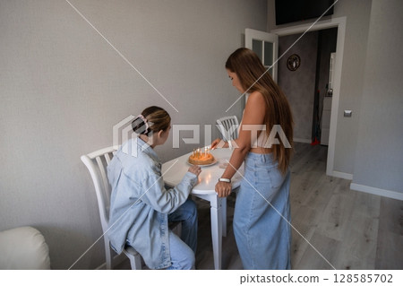 Women Apartment Snack: Two young women sharing a snack at a small table inside an apartment, likely for a casual meal or break. Women Apartment Snack: Two young women sharing a snack at a small table inside an apartment, likely for a casual meal or break. 128585702