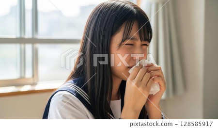 一名身穿制服的女高中生在教室裡用紙巾擤鼻涕 128585917