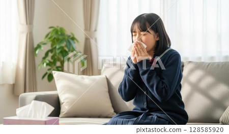 A high school girl blowing her nose painfully on the living room sofa 128585920