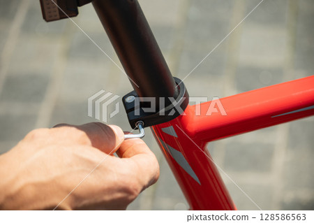 Close up of hands adjusts red bicycle seat using hex key, ensuring comfortable ride. Bicycle mechanic assembling braking and shifting system of bike as part of maintenance service. Close up of hands adjusts red bicycle seat using hex key, ensuring comfortable ride. Bicycle mechanic assembling braking and shifting system of bike as part of maintenance service. 128586563