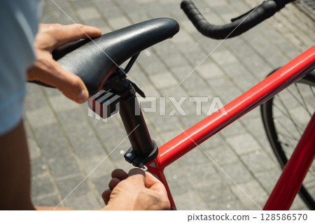 Close up of hands adjusts red bicycle seat using hex key, ensuring comfortable ride. Bicycle mechanic assembling braking and shifting system of bike as part of maintenance service. Close up of hands adjusts red bicycle seat using hex key, ensuring comfortable ride. Bicycle mechanic assembling braking and shifting system of bike as part of maintenance service. 128586570