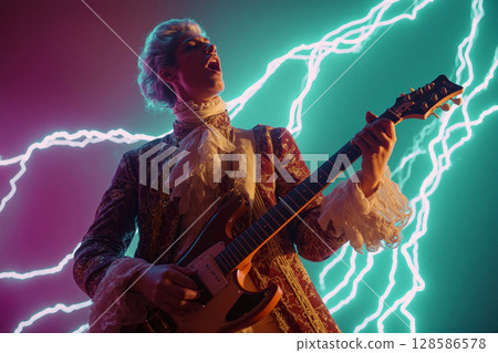 Performer plays electric guitar with vibrant lightning backdrop during lively music event at night 128586578