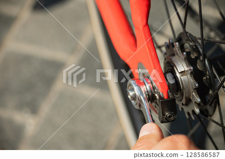 Close up of hands using wrench to tighten rear gear of red bicycle. Bicycle repair and maintenance. 128586587