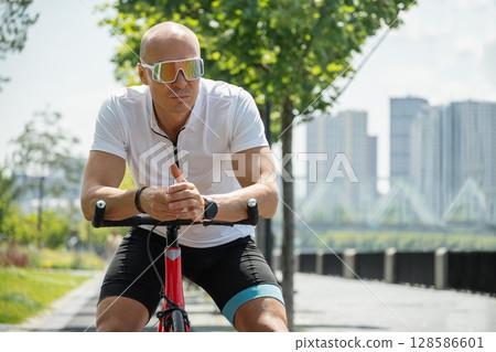 Handsome caucasian cyclist relax on bicycle at summer public park. Carbon Footprint. Eco transport. Lower Energy Consumption. Man leaning on racing bicycle in park. 128586601