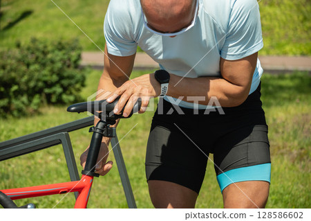 Man adjusting bicycle seat with hex key tool at nature public park. Summer activity. Man adjusting bicycle seat with hex key tool at nature public park. Summer activity. 128586602