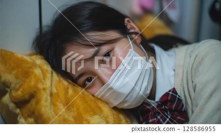 一名高中女生因感冒戴著口罩躺在家裡的床上 一名高中女生因感冒戴著口罩躺在家裡的床上 128586955