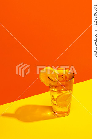 Citrus sparkling drink with lemon slices in highball glass on yellow and orange background Citrus sparkling drink with lemon slices in highball glass on yellow and orange background 128586971