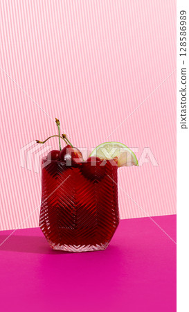 Red sleepy girl mocktail with cherries and lime on striped pink backdrop 128586989