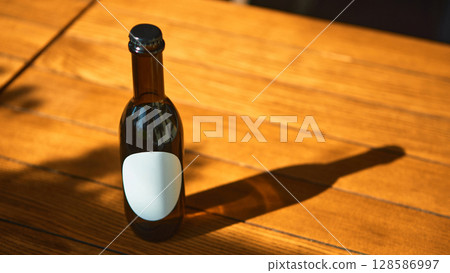 Blank label brown bottle on wooden table for promotional mockup in warm lighting 128586997