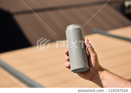 Matte grey drink can held in male hand with rooftop in soft background light 128587026