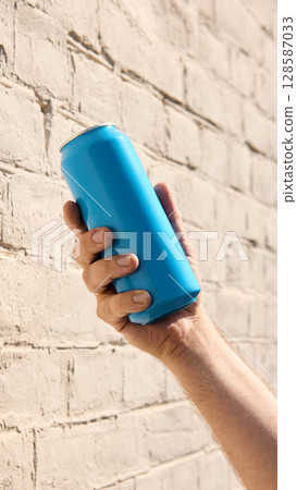 Hand holding cyan blue drink can near brick wall for branding mockup 128587033