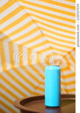 Cyan blue drink can standing on table with yellow striped umbrella background. Mockup for ads, text 128587034