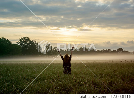 Back view of a person reaching for the sky in a grassland and a cloudy sky 128588116