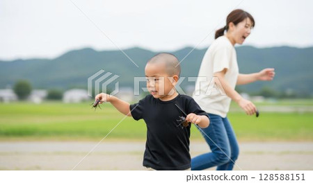 A proud boy holding a rhinoceros beetle in each hand and his surprised mother 128588151