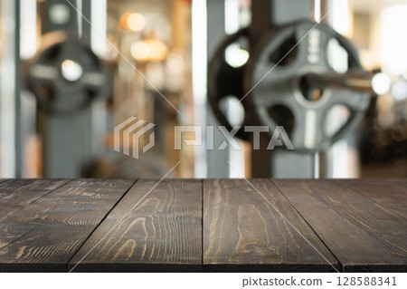 Empty wooden table top and blurred gym or fitness center as background. Empty wooden table top and blurred gym or fitness center as background. 128588341