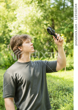 Overheated handsome young man with hand electric fan suffering from heat at park. Heat Summer. Handheld fan. Beat heat. Overheated handsome young man with hand electric fan suffering from heat at park. Heat Summer. Handheld fan. Beat heat. 128588344