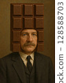 A satirical and humorous concept art of a man in a suit wearing a chocolate bar headgear and standing with a blank expression 128588703