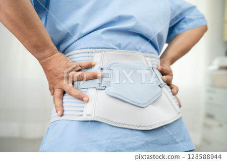 Asian woman patient wearing back pain support belt for orthopedic lumbar with walker. Asian woman patient wearing back pain support belt for orthopedic lumbar with walker. 128588944