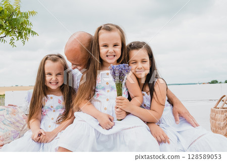 On a white wooden bench, the father embraces his three daughters On a white wooden bench, the father embraces his three daughters 128589053