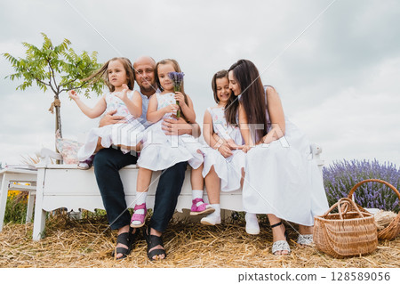 A close-knit family sits on an old-fashioned bench in a picturesque field A close-knit family sits on an old-fashioned bench in a picturesque field 128589056