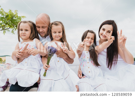 A beautiful family sits on a wooden bench in a flower field A beautiful family sits on a wooden bench in a flower field 128589059