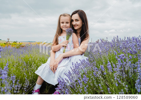 Young mother holds her little daughter in her arms, sitting in the middle of a charming lavender field 128589060