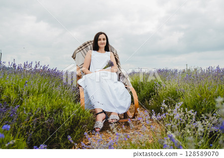 A girl in a white dress sits on a rocking chair in the middle of a lavender field 128589070