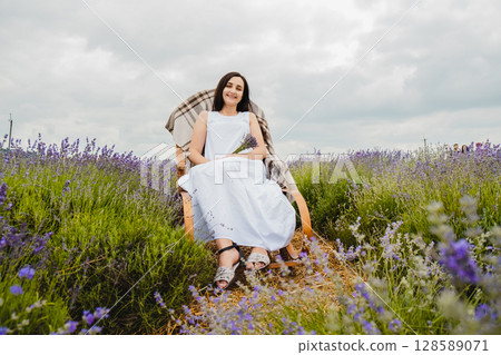 In the lavender field, a young woman in a white dress is sitting 128589071