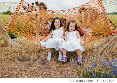 Two girls in white dresses are swinging on a red mesh hammock Two girls in white dresses are swinging on a red mesh hammock 128589198