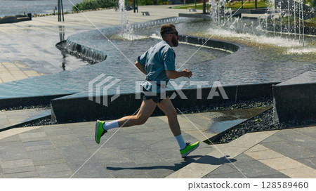 Midlife man jogging beside urban fountains on sunny day Midlife man jogging beside urban fountains on sunny day 128589460
