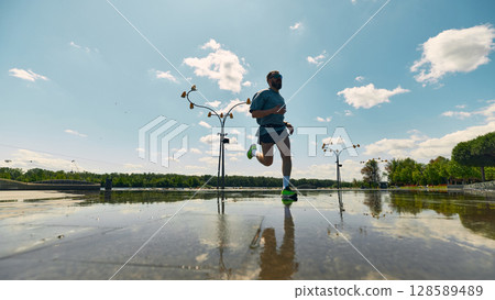 Midlife man jogging on sunny day near river with clear sky and clouds 128589489