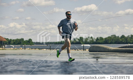 Man jogging on waterfront under cloudy blue sky promoting midlife fitness 128589578