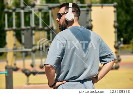 Man with headphones relishing exercise session at open-air fitness park Man with headphones relishing exercise session at open-air fitness park 128589588