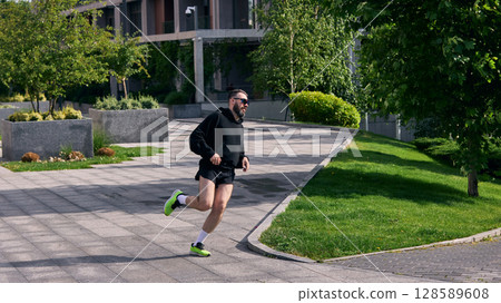 Middle aged man jogging in urban park under sunny sky near modern building Middle aged man jogging in urban park under sunny sky near modern building 128589608