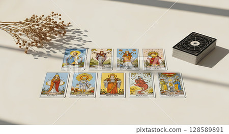 Ten tarot cards laid out in two rows on a surface with dried flowers nearby; a stack of cards with an intricate design rests on the right side, casting shadows across the scene 128589891