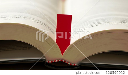 Open book with a red bookmark at the center, pages slightly curved, creating an inviting and warm aesthetic. Text is visible, lines of black letters fill the pages, binding in focus 128590012