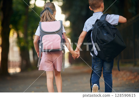 Back view, walking. Young school children of boy and girl are together outdoors 128590615