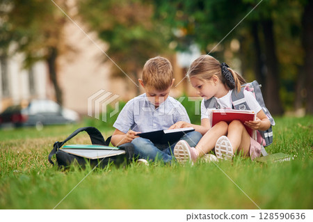 Sitting on the green grass. Young school children of boy and girl are together outdoors 128590636