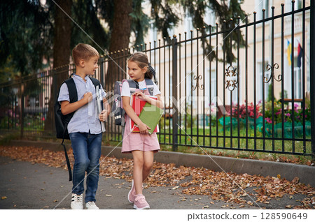 Holding notebook and books. Young school children of boy and girl are together outdoors Holding notebook and books. Young school children of boy and girl are together outdoors 128590649