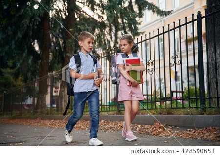 Holding notebook and books. Young school children of boy and girl are together outdoors Holding notebook and books. Young school children of boy and girl are together outdoors 128590651