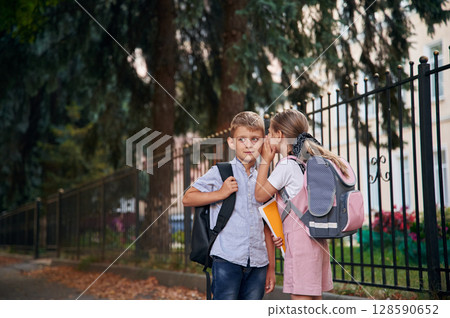 To gossip. Young school children of boy and girl are together outdoors 128590652