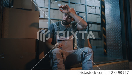 Tired Worker Carrying Cardboard Box with Online Order, Having Break, Using Smartphone 128590967