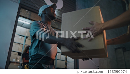 Outside of Logistics Distribution Warehouse at Night: Worker Giving Cardboard Box to Colleague Outside of Logistics Distribution Warehouse at Night: Worker Giving Cardboard Box to Colleague 128590974